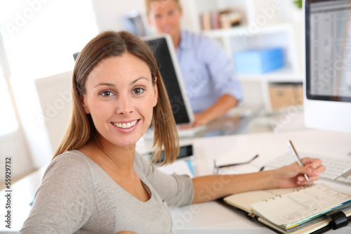Photo: Young businesswoman sitting at desk in office Young businesswoman sitting at desk in office
