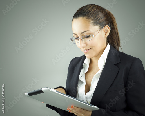 Photo: Smiling woman holding a tablet computer over grey background Smiling woman holding a tablet computer over grey background