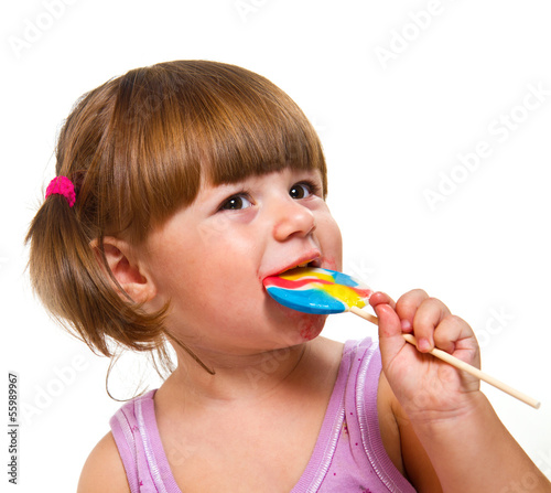 Photo: Cute little girl eating a colored lollipop Cute little girl eating a colored lollipop