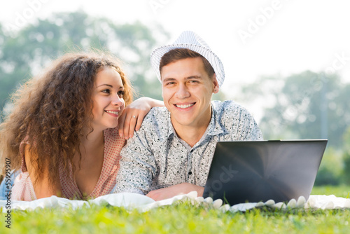 Photo: couple lying together in a park with laptop couple lying together in a park with laptop