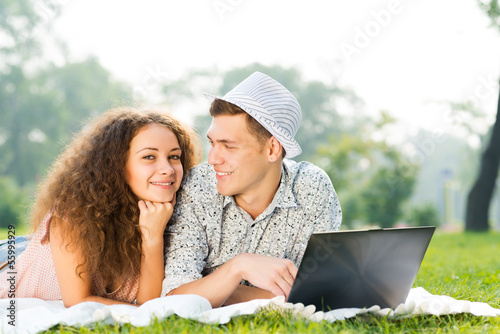 Photo: couple lying together in a park with laptop couple lying together in a park with laptop