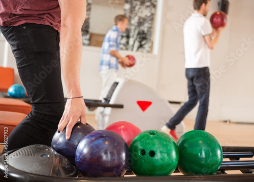 Photo: Man Picking Bowling Ball With Friends in Background Man Picking Bowling Ball With Friends in Background