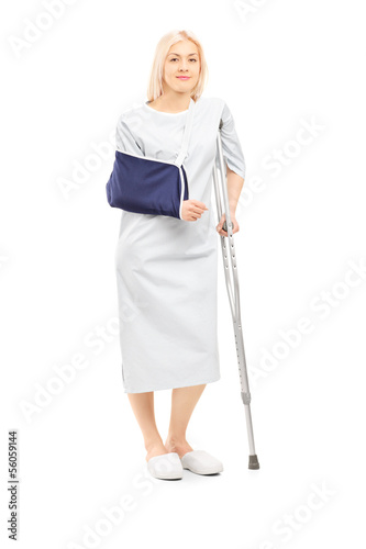 Photo: Blond female patient in gown with broken arm and crutch Blond female patient in gown with broken arm and crutch