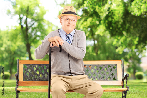 Photo: Senior man sitting on a wooden bench, in a park Senior man sitting on a wooden bench, in a park