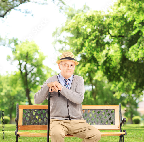 Photo: Senior man sitting on a bench and looking at camera, in a park Senior man sitting on a bench and looking at camera, in a park
