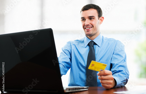Photo: Man using a credit card in front of his laptop Man using a credit card in front of his laptop