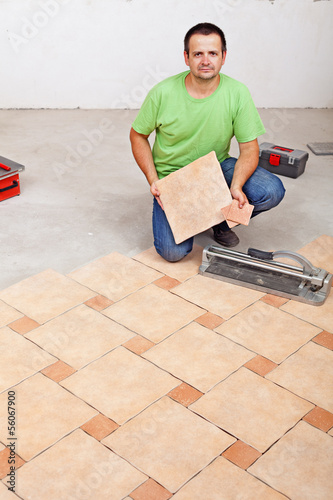 Photo: Worker laying floor tiles on concrete surface Worker laying floor tiles on concrete surface