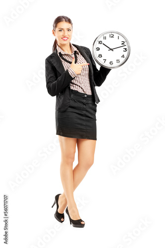Photo: Smiling female standing and pointing on a wall clock Smiling female standing and pointing on a wall clock