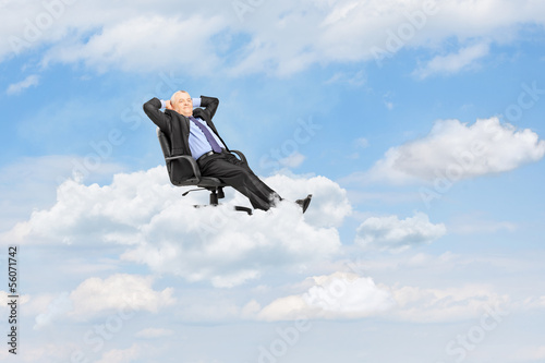 Photo: Mature businessman resting in armchair and floating on a cloud Mature businessman resting in armchair and floating on a cloud