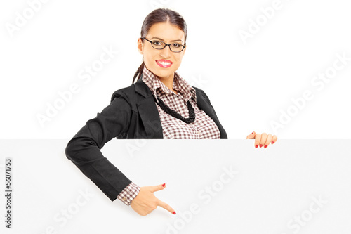 Photo: Smiling beautiful woman in suit pointing on a blank panel Smiling beautiful woman in suit pointing on a blank panel