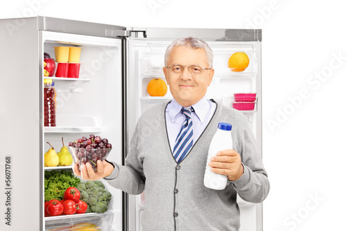 Photo: Mature man holding a bottle and grapes next to a fridge Mature man holding a bottle and grapes next to a fridge