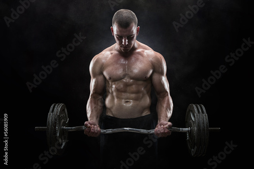 Photo: Young muscular man lifting weights over dark background Young muscular man lifting weights over dark background