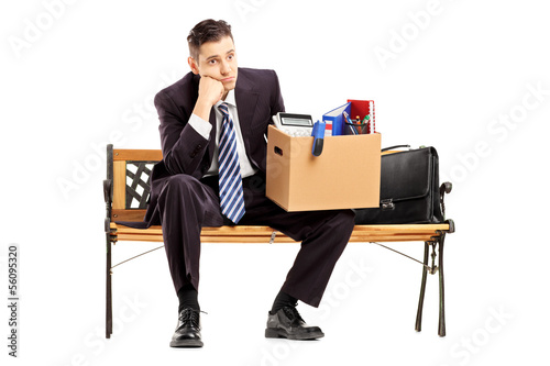 Photo: Disappointed businessman in a suit sitting on a bench with a box Disappointed businessman in a suit sitting on a bench with a box