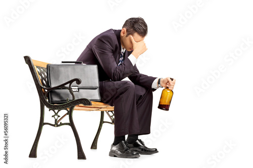 Photo: Disappointed businessperson sitting on a bench with a bottle Disappointed businessperson sitting on a bench with a bottle