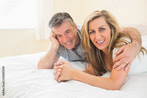 Photo: Happy couple lying on a bed looking at camera Happy couple lying on a bed looking at camera