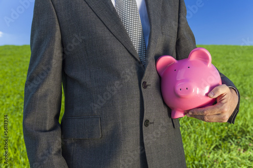 Photo: Man Businessman Holding Piggy Bank in Field Man Businessman Holding Piggy Bank in Field