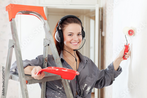 Photo: Happy woman in headphones paints wall Happy woman in headphones paints wall