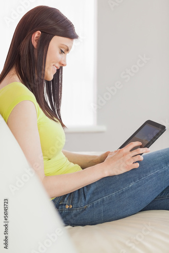 Photo: Happy girl sitting on a sofa using a tablet pc Happy girl sitting on a sofa using a tablet pc