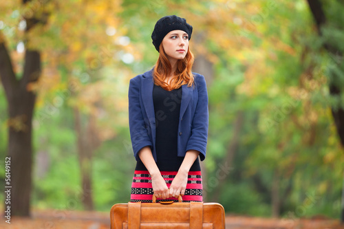 Photo: Redhead girl with suitcase at autumn outdoor. Redhead girl with suitcase at autumn outdoor.