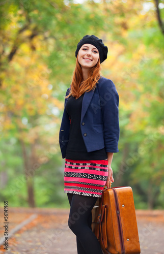 Photo: Redhead girl with suitcase at autumn outdoor. Redhead girl with suitcase at autumn outdoor.