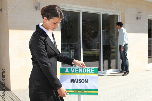 Photo: Woman placing home for sale sign Woman placing home for sale sign