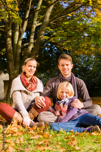 Photo: Happy Family outdoors sitting on grass in autumn Happy Family outdoors sitting on grass in autumn