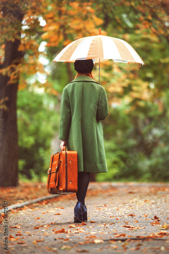 Photo: Redhead girl with suitcase at autumn outdoor. Redhead girl with suitcase at autumn outdoor.