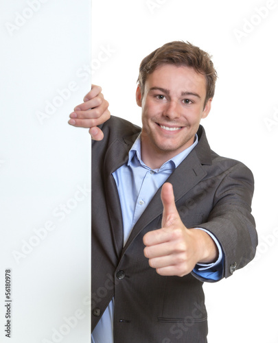 Photo: Young businessman showing thumb behind a signboard Young businessman showing thumb behind a signboard