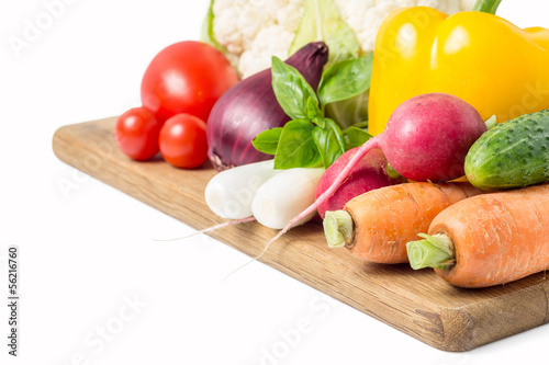 Photo: Fresh vegetables at wood cutting board isolated on white Fresh vegetables at wood cutting board isolated on white