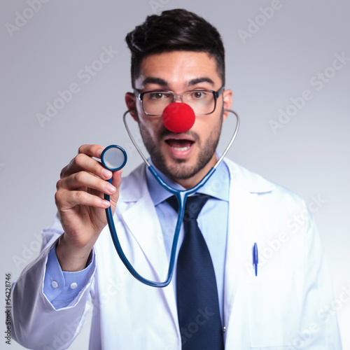 Photo: young doctor listens to you at stethoscope with red nose young doctor listens to you at stethoscope with red nose