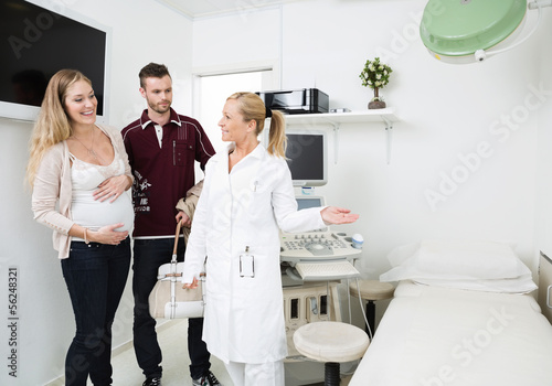 Photo: Doctor Gesturing While Looking At Expectant Couple Doctor Gesturing While Looking At Expectant Couple