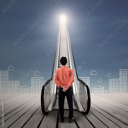 Photo: Businessman at escalator under bright sky Businessman at escalator under bright sky