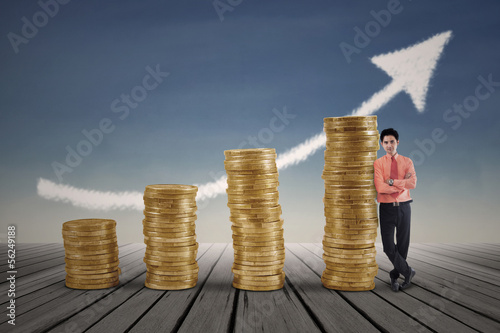 Photo: Businessman standing next to gold coins growth chart Businessman standing next to gold coins growth chart