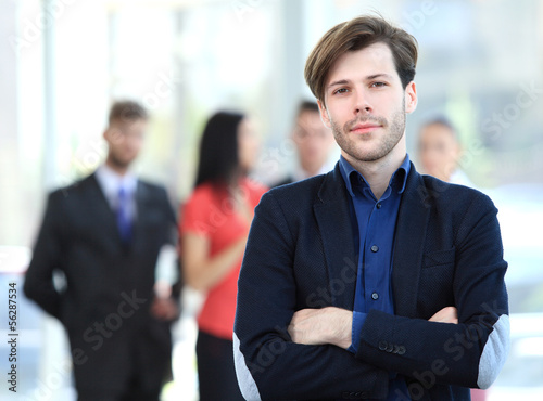 Photo: Handsome happy business man with colleagues at the back Handsome happy business man with colleagues at the back