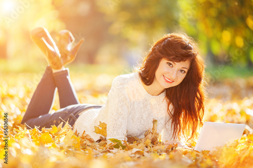 Photo: Cute woman with white laptop in the autumn park Cute woman with white laptop in the autumn park