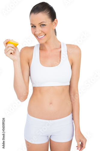 Photo: Smiling woman in sportswear holding slice of orange looking at c Smiling woman in sportswear holding slice of orange looking at c