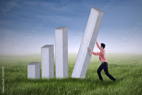 Photo: Young businessman pushing a bar chart outdoor Young businessman pushing a bar chart outdoor