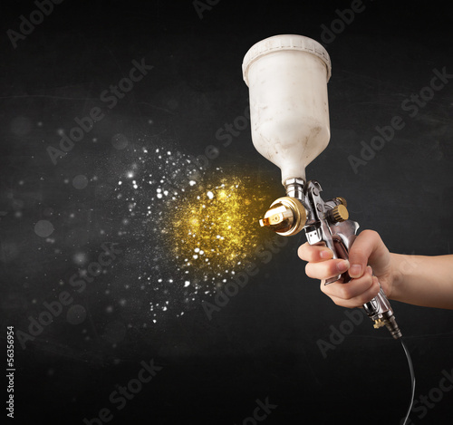 Photo: Worker with airbrush painting with glowing golden paint Worker with airbrush painting with glowing golden paint