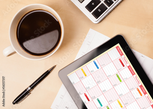 Photo: Tablet pc showing calendar on screen with a cup of coffee on a d Tablet pc showing calendar on screen with a cup of coffee on a d
