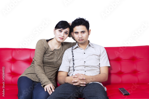 Photo: Unhappy couple watching TV and sitting on red sofa Unhappy couple watching TV and sitting on red sofa