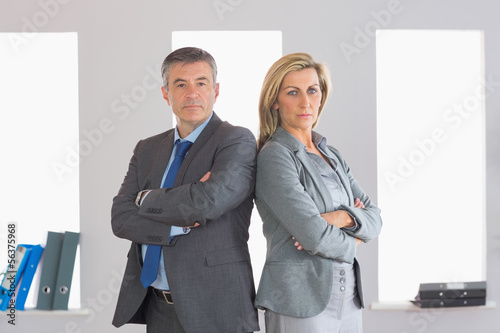 Photo: Two unsmiling businesspeople looking at camera standing back to Two unsmiling businesspeople looking at camera standing back to