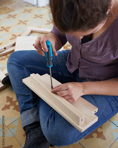 Photo: Young woman building piece of furniture Young woman building piece of furniture