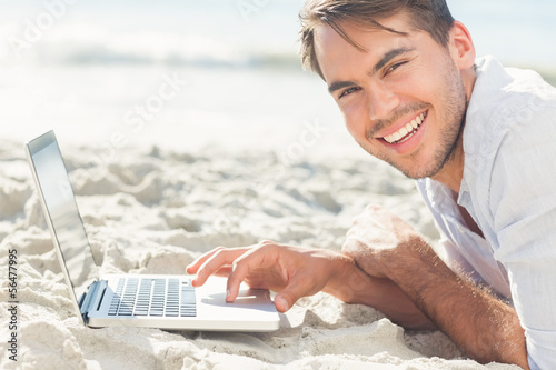 Photo: Smiling handsome man on the beach using his laptop Smiling handsome man on the beach using his laptop