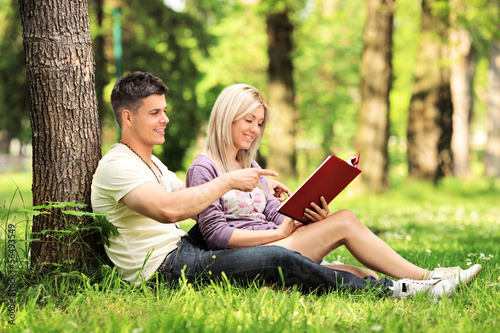 Photo: Heterosexual couple sitting and reading a novel in a park Heterosexual couple sitting and reading a novel in a park