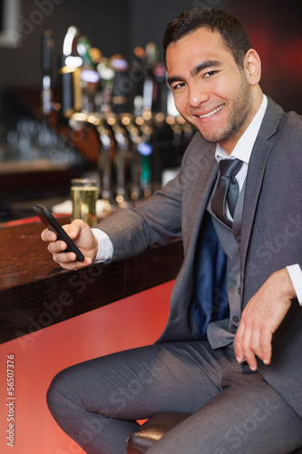 Photo: Cheerful businessman sending a text while having a drink Cheerful businessman sending a text while having a drink