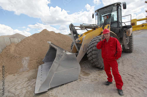 Photo: worker in red uniform on phone, buldozer in background worker in red uniform on phone, buldozer in background