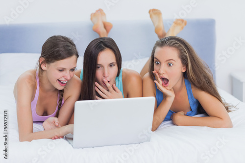 Photo: Grils on bed looking at laptop Grils on bed looking at laptop