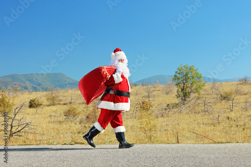 Photo: Santa claus with bag walking on an open road Santa claus with bag walking on an open road