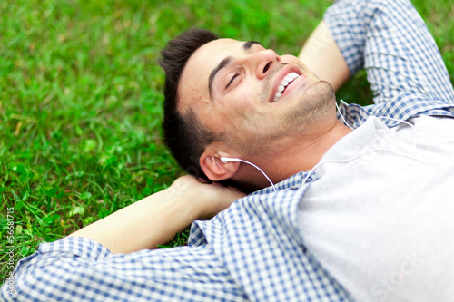 Photo: Young man listening to music lying on the grass Young man listening to music lying on the grass