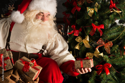 Photo: Santa putting gifts under Christmas tree in dark room Santa putting gifts under Christmas tree in dark room